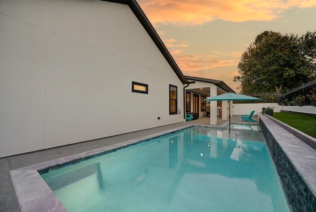 pool at dusk with a patio area and an in ground hot tub