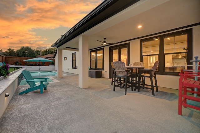 patio terrace at dusk with ceiling fan and a fenced in pool