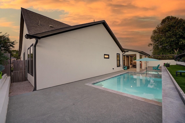 pool at dusk with a fenced backyard, a pool with connected hot tub, and a patio