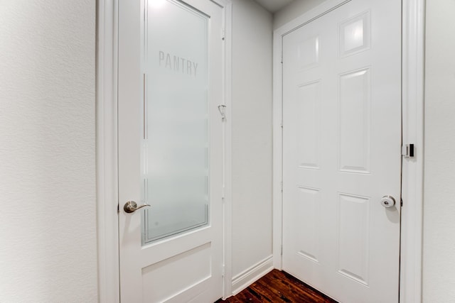 doorway featuring baseboards, dark wood finished floors, and a textured wall