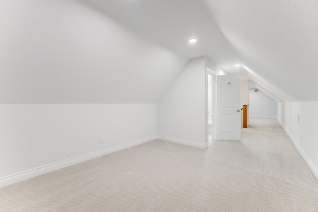 additional living space featuring light colored carpet and vaulted ceiling