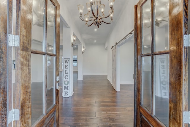 hallway with a barn door, dark hardwood / wood-style floors, and an inviting chandelier