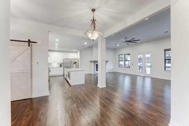 unfurnished living room with ceiling fan, sink, dark hardwood / wood-style flooring, and a barn door