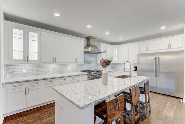 kitchen featuring wall chimney range hood, a kitchen bar, sink, high end appliances, and a kitchen island with sink