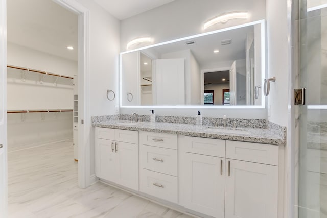 bathroom with double vanity, marble finish floor, a walk in closet, and a sink