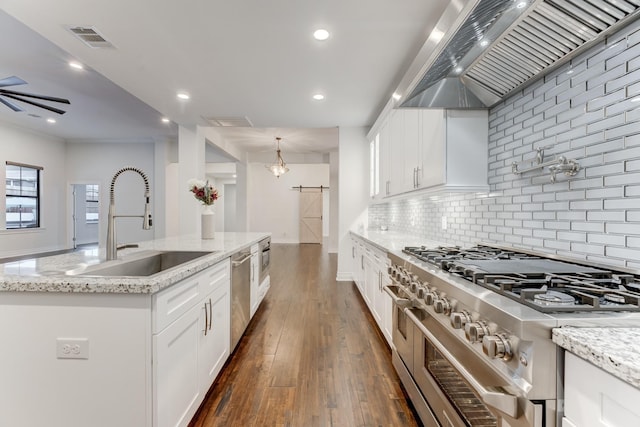 kitchen featuring white cabinets, a barn door, wall chimney exhaust hood, and stainless steel appliances