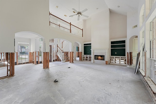 unfurnished living room featuring concrete flooring, a towering ceiling, and ceiling fan