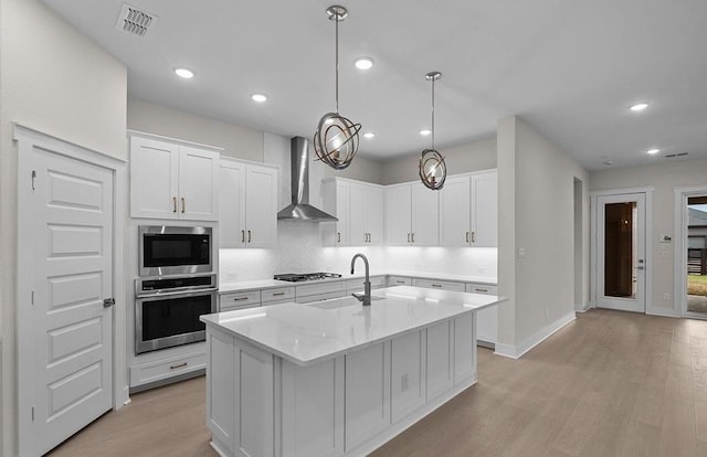 kitchen with built in microwave, wall chimney range hood, a center island with sink, white cabinetry, and oven