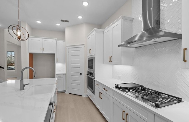 kitchen featuring white cabinets, wall chimney exhaust hood, and decorative light fixtures