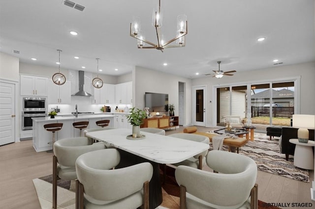 dining space featuring ceiling fan with notable chandelier, light hardwood / wood-style flooring, and sink