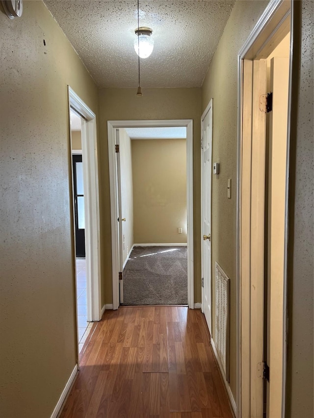 corridor with wood-type flooring and a textured ceiling