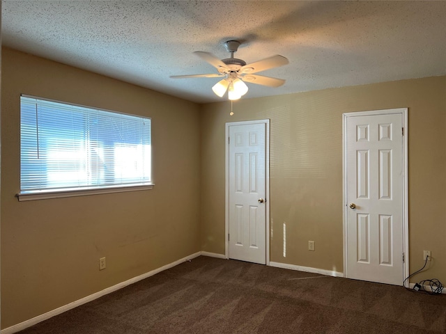 unfurnished bedroom featuring ceiling fan, dark carpet, and a textured ceiling