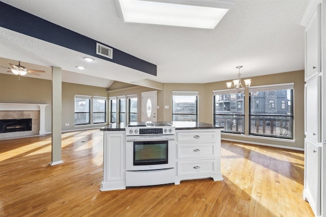 kitchen with light hardwood / wood-style flooring, a tile fireplace, white cabinetry, hanging light fixtures, and electric range