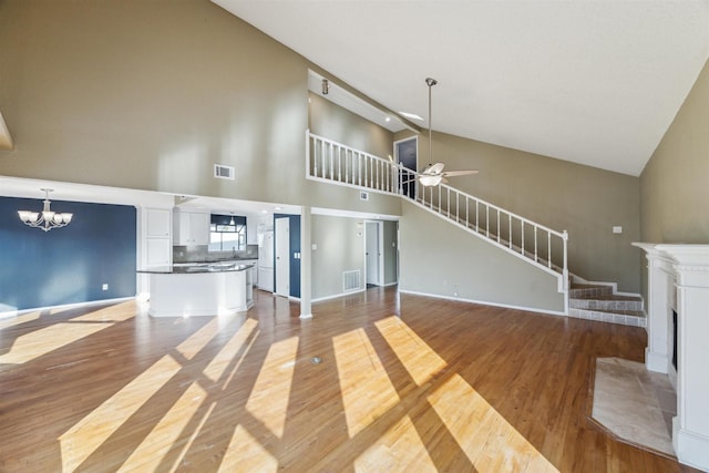 unfurnished living room with ceiling fan with notable chandelier, high vaulted ceiling, and light hardwood / wood-style flooring