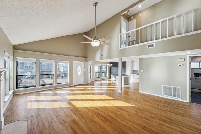 unfurnished living room featuring vaulted ceiling, ceiling fan with notable chandelier, a textured ceiling, and light wood-type flooring