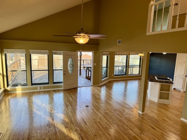 unfurnished living room featuring ceiling fan, high vaulted ceiling, a healthy amount of sunlight, and light wood-type flooring