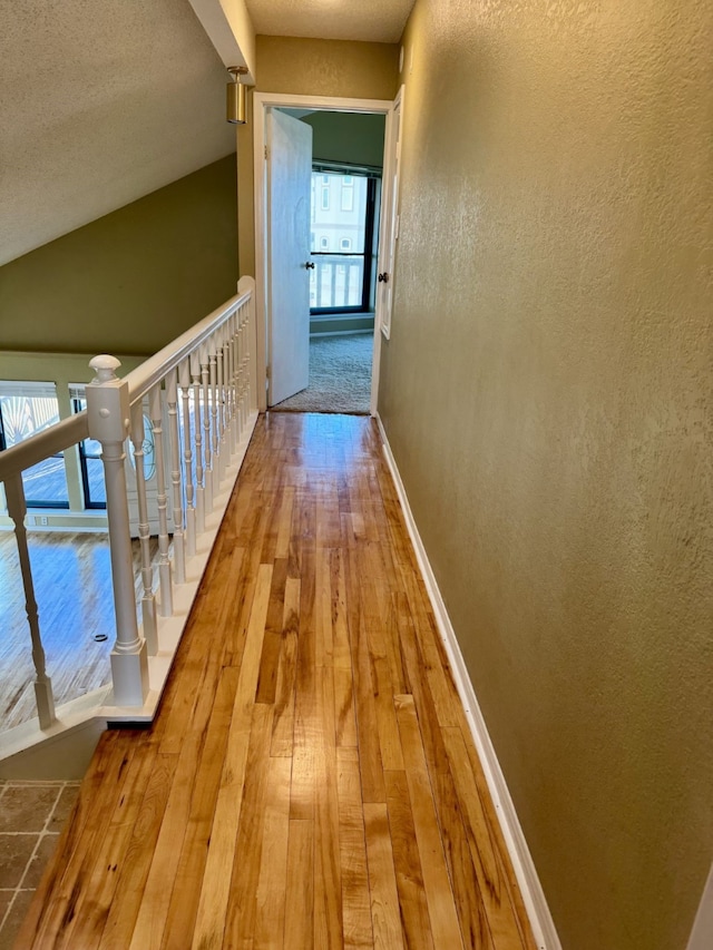 corridor with lofted ceiling, wood-type flooring, and a textured ceiling