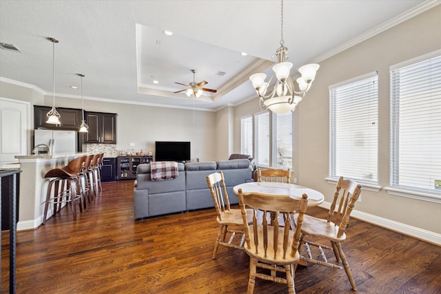 dining space featuring dark hardwood / wood-style floors, ornamental molding, ceiling fan with notable chandelier, and a tray ceiling