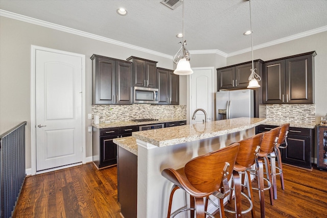 kitchen featuring dark hardwood / wood-style floors, decorative light fixtures, a kitchen island with sink, a breakfast bar, and appliances with stainless steel finishes