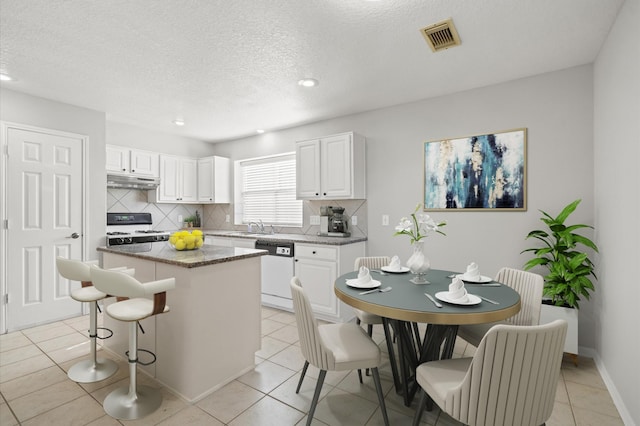 kitchen featuring black gas range, white cabinetry, light tile patterned floors, white dishwasher, and a kitchen island