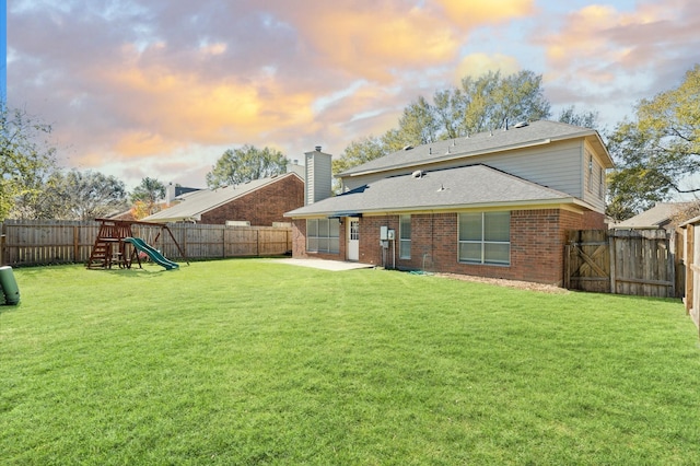 back house at dusk featuring a playground, a patio area, and a lawn