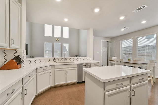 kitchen featuring white cabinets, sink, light hardwood / wood-style flooring, stainless steel dishwasher, and a kitchen island