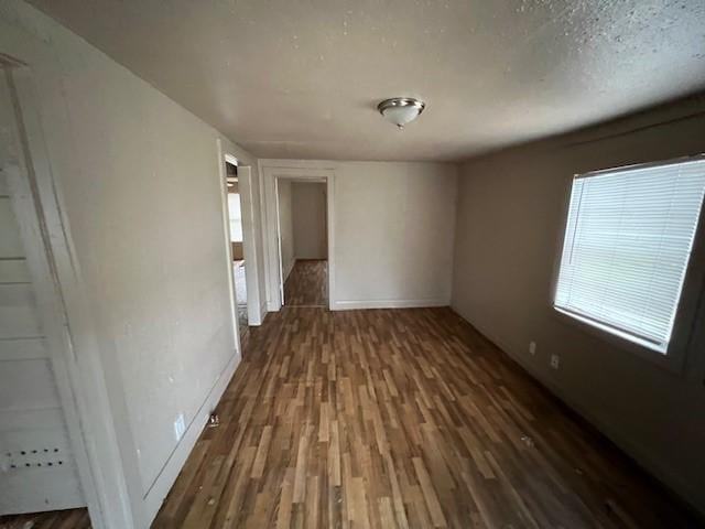 empty room featuring a textured ceiling, dark wood-type flooring, and a healthy amount of sunlight