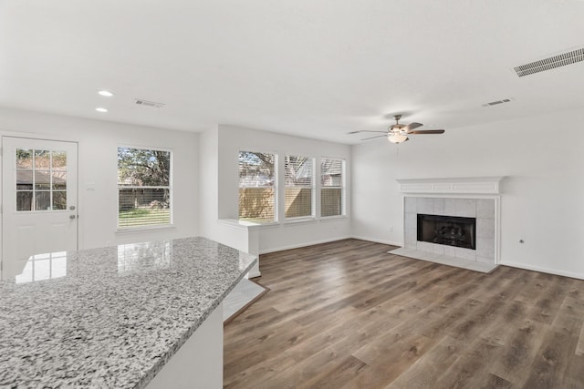 unfurnished living room featuring a tile fireplace, ceiling fan, and dark wood-type flooring