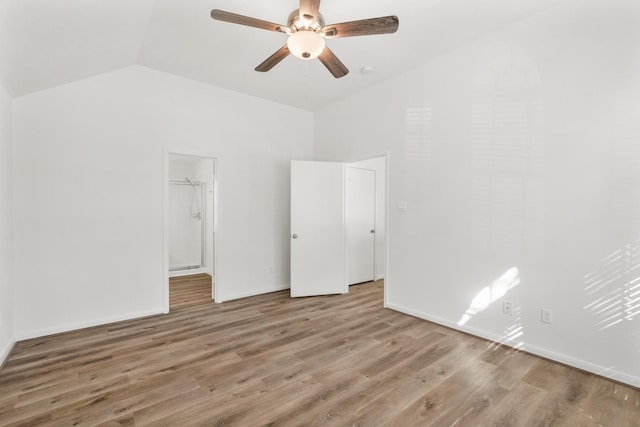 unfurnished bedroom featuring vaulted ceiling, ceiling fan, wood-type flooring, a spacious closet, and a closet