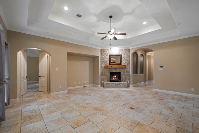 unfurnished living room featuring ceiling fan, ornamental molding, a tray ceiling, and a stone fireplace