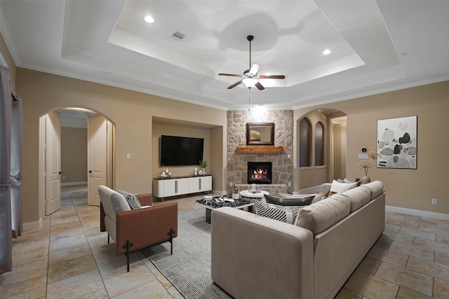 living room with ceiling fan, a fireplace, ornamental molding, and a tray ceiling