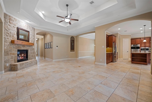 unfurnished living room with a tray ceiling, crown molding, a fireplace, and ceiling fan