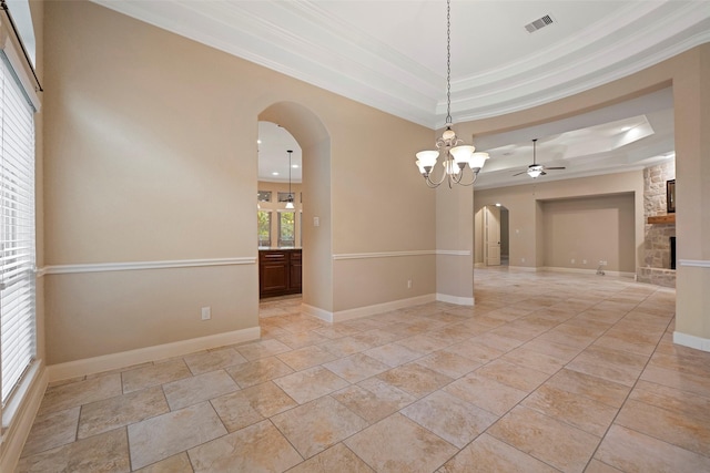 unfurnished room with ceiling fan with notable chandelier, a fireplace, ornamental molding, and a raised ceiling