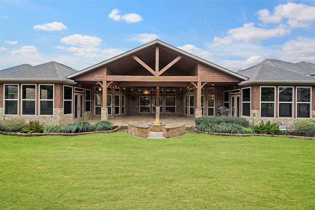 rear view of property with a fire pit, a patio, stone siding, roof with shingles, and a yard