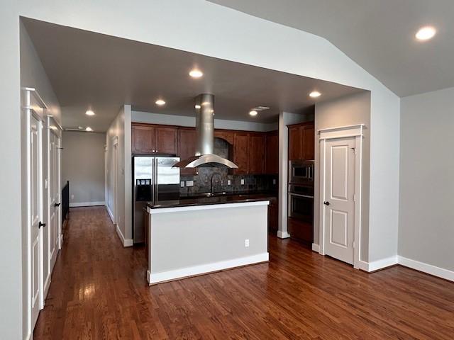 kitchen with backsplash, vaulted ceiling, island range hood, a kitchen island, and appliances with stainless steel finishes