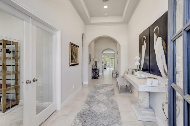 corridor with a raised ceiling, light tile patterned floors, and french doors