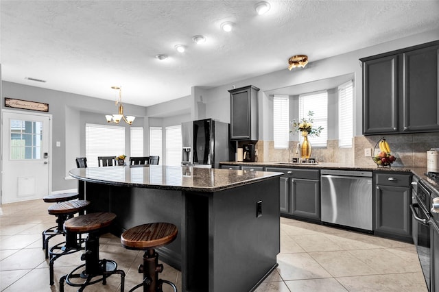 kitchen featuring black fridge, dark stone counters, pendant lighting, dishwasher, and a kitchen island