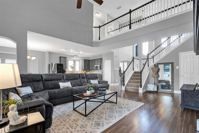 living room featuring ceiling fan with notable chandelier, dark wood-type flooring, and a high ceiling