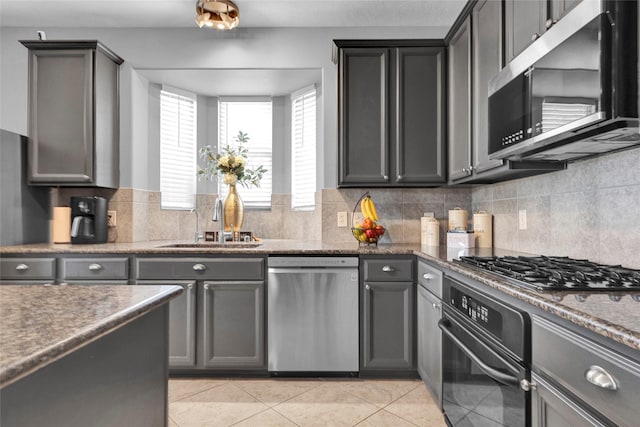 kitchen featuring tasteful backsplash, stainless steel appliances, sink, light tile patterned floors, and dark stone countertops