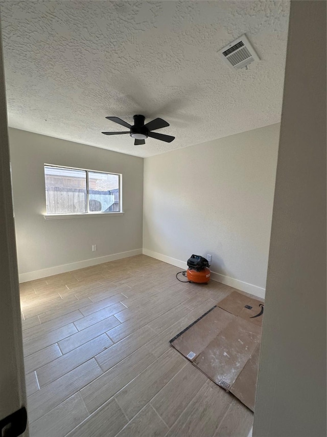 spare room featuring ceiling fan, light wood-type flooring, and a textured ceiling