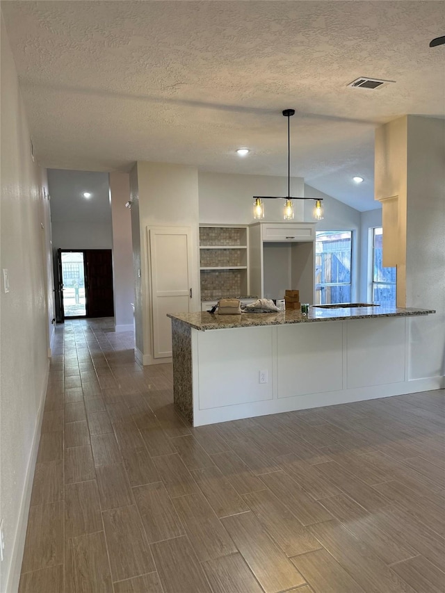 kitchen with stone countertops, lofted ceiling, white cabinets, decorative light fixtures, and kitchen peninsula