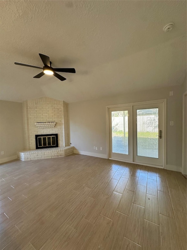 unfurnished living room with a textured ceiling, a brick fireplace, ceiling fan, and lofted ceiling