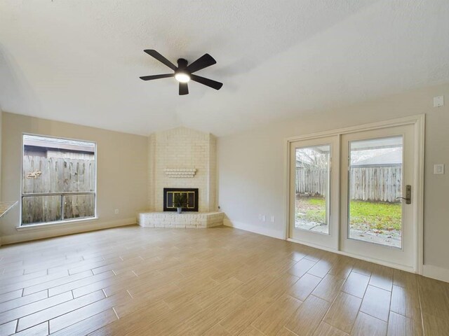 unfurnished living room with vaulted ceiling, a brick fireplace, ceiling fan, and light wood-type flooring