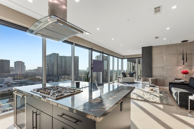 kitchen featuring a wealth of natural light, island range hood, stainless steel gas stovetop, and dark stone counters