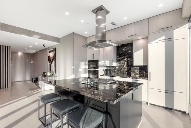 kitchen with a breakfast bar, backsplash, dark stone counters, a large island, and island exhaust hood