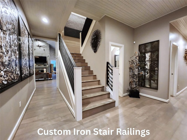 stairway with ceiling fan, wooden ceiling, wood-type flooring, and a fireplace