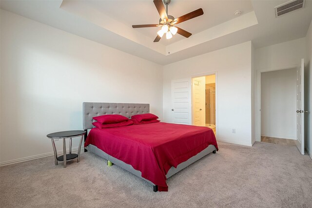 carpeted bedroom with a raised ceiling, ensuite bath, and ceiling fan