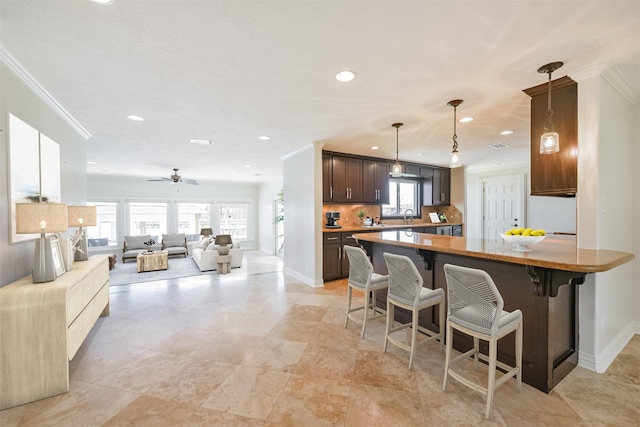 kitchen featuring dark brown cabinetry, ceiling fan, sink, a kitchen breakfast bar, and decorative light fixtures