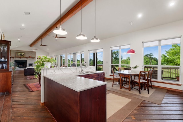 kitchen with a kitchen island with sink, lofted ceiling with beams, sink, decorative light fixtures, and light stone counters