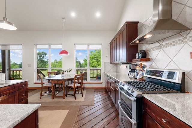 kitchen featuring light stone countertops, wall chimney exhaust hood, hanging light fixtures, stainless steel range oven, and backsplash